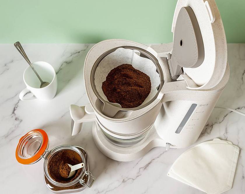 Preparing auto drip coffee with coffee bed filled with coffee grounds in a white automatic coffee maker